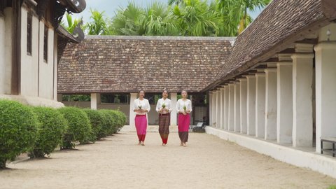 A group of northern Thai young Asian women with traditional Lanna costume holding flowers, walking at Wat Ton Kwen or Wat Inthrawat, Chiang Mai, Thailand. People lifestyle