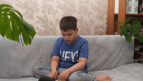 Happy boy lying on sofa at home and playing with pc tablet. Joyful boy playing video games and laughing. teenager watching cartoons or a movie at home. Chatting with friends online. Learning online.