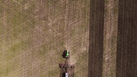 Aerial top view of Tractor plowing and fertilizing the agricultural fields in the springtime. Drone video with the follow camera