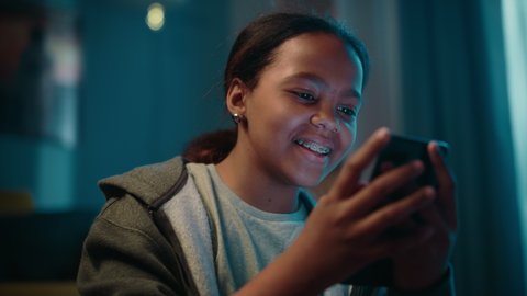 Portrait of a Teenage Multiethnic Black Girl Using a Smartphone. Young Female Browses Internet, Checks Social Media, Chats with Friends. She Wears Dental Braces.