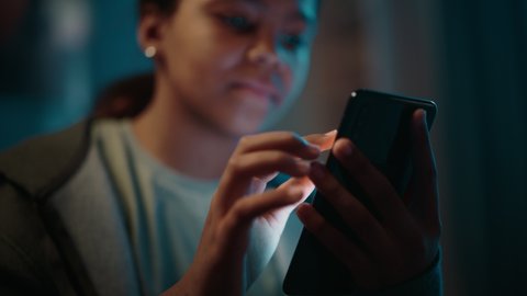 Portrait of a Teenage Multiethnic Black Girl Using a Smartphone. Young Female Browses Internet, Checks Social Media, Chats with Friends. She Wears Dental Braces.