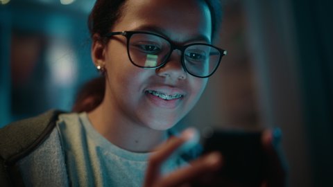 Portrait of a Teenage Multiethnic Black Girl Using a Smartphone. Young Female Browses Internet, Checks Social Media, Chats with Friends. She Wears Glasses and Dental Braces.