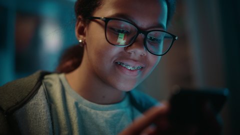 Portrait of a Teenage Multiethnic Black Girl Using a Smartphone. Young Female Browses Internet, Checks Social Media, Chats with Friends. She Wears Glasses and Dental Braces.