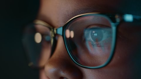 Close Up Portrait of a Cute Young Teenage Multiethnic Black Girl in a Dark Cozy Room at Home. Young Female Wears Glasses that Reflect School Homework from Her Laptop Computer Screen in Them.