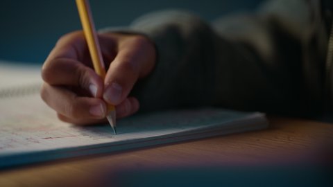 Authentic Close Up Footage of a Young Teenage Girl with Glasses Writing with Pencil in Notebook. Teenager Making Homework for School. Education Concept.