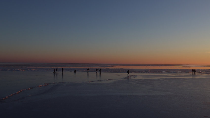 The frozen lake in winter on sunset. Children and adults have fun walking and rolling on ice-covered water.