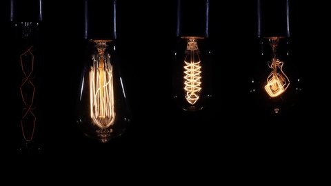 A set of several pulsating incandescent lamps as a background for video editing. Set of filament lamp with a tungsten spiral pendant lantern lights up and goes out on a black backdrop.