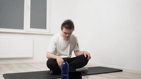 A young sports guy performs exercises on a black mat, repeating what is happening on the tablet, he does exercises to strengthen the body and spirit. Home workout concept, yoga