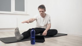 A young sports guy performs exercises on a black mat, repeating what is happening on the tablet, he does exercises to strengthen the body and spirit. Home workout concept, yoga