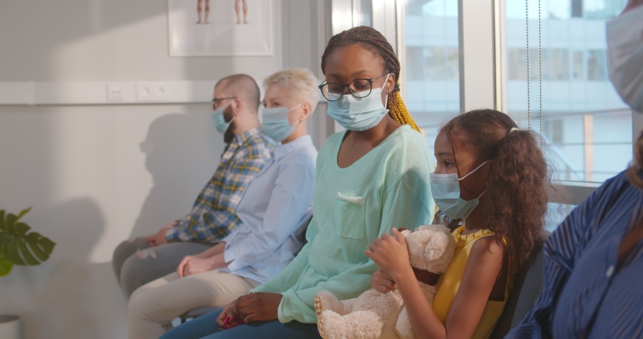 African doctor inviting patients in hospital waiting-room for coronavirus vaccination. Diverse people wearing safety mask sitting in clinic reception area waiting for appointment | Shutterstock HD Video #1073628614