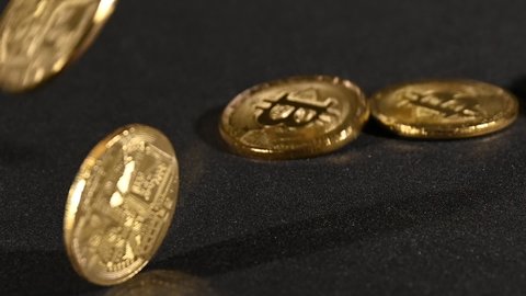 Close up golden bitcoin physical coins fall down and bounce over black background with copy space, high angle view, slow motion