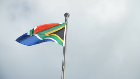 South African flag in left of frame against cloudy sky waving in the wind on bright day