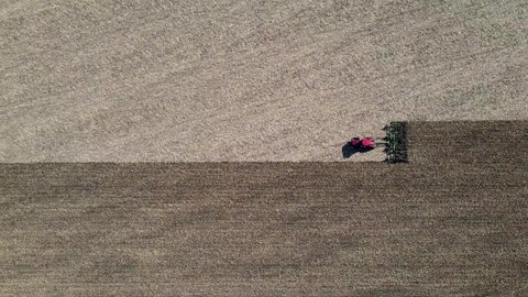 Aerial view of red tractor tilling center of farm field in the fall, sharp contrast shown on land. Driving horizontally across frame. North Dakota. Outdoors.