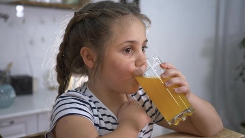 Little girl drinks juice. Organic fruit drink. Girl with glass of orange juice. Organic healthy juice. Little girl at home with drink. Child drinks juice. Organic healthy products concept.
