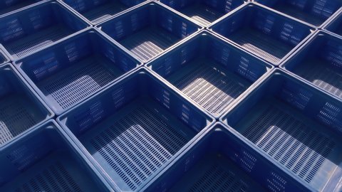 Unbranded storage plastic container crates drone shot at an outdoors area. Aerial day view panning above many stacked blue multipurpose empty crates. 