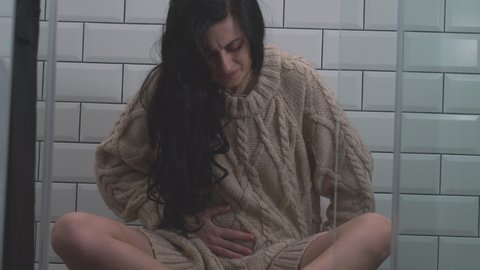 close up of a young girl with beautiful long hair holding her belly sitting on the floor and suffering from debilitating pain during PMS