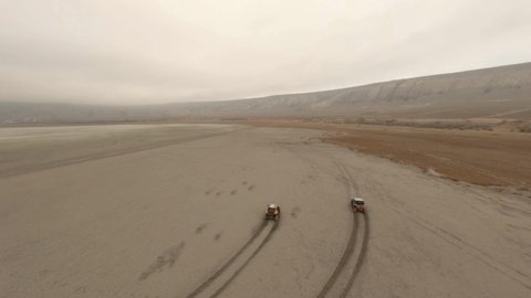 Aerial follow shot two extreme buggy car racing sandy desert surrounded by dirt dust and smog top view. Shooting from sport fpv drone chase rally automobile race extreme recreational outdoor activity