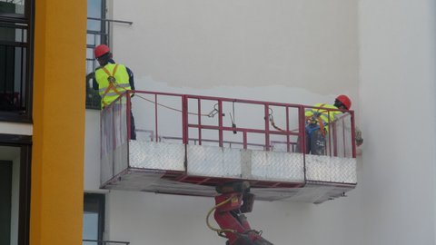 SAINT PETERSBURG, RUSSIA - CIRCA APRIL, 2021: Workers at height in construction cradle painting the wall of a multi-storey building