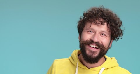 close up of cool unshaved hipster guy showing glasses, being surprised, taking a step back and getting scared, laughing and having fun on blue background in studio