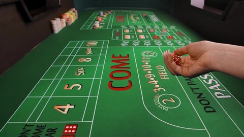 A female hand throws dice on a green craps table in a casino. Close up of a gaming table with placed chips. The concept of gambling business. Slow motion.