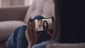 Young Asian female sitting on the sofa and using smartphone video call talking with friends while living at home. Self-isolation, social distancing, quarantine at home.