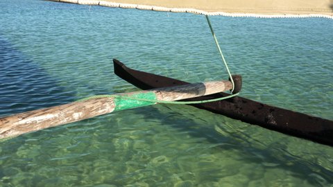 Looking to wooden pole and board of pirogue - typical Madagascar small fishing boat - sailing over clear green sea water
