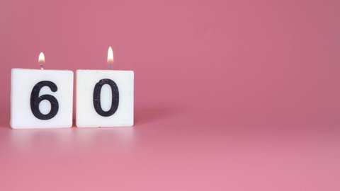 A square candle saying the number 60 being lit and blown out on a pink background celebrating a birthday or anniversary 