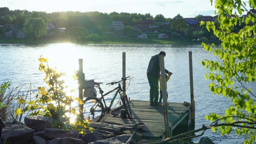 
Dad and daughter at sunset on the pier of the lake. Old pier on a forest lake. Evening bike ride. Daddy