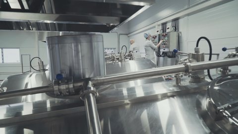 Two Female Operators In Masks Observing Dairy Production Process. Using Control Panel, Checking Up, Communicating With A Colleague. Curd Manufacturing At A Modern Plant. Diary Food manufacture.