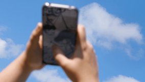 Against the blue sky, a woman's hand is holding a phone. He taps the screen with his finger. Video out of focus