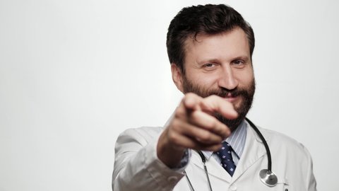 Doctor points his finger to you. Smiling kind man doctor on white background looking at camera and points his finger in camera