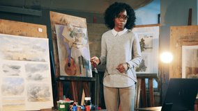 African ethnicity lady is explaining a painting during an online art lesson