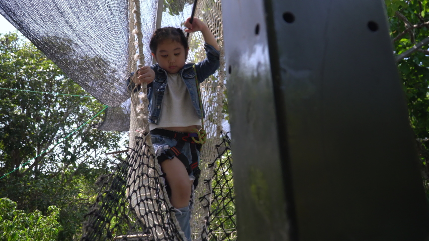 Happy asian Little Girl climbing on rope nets on playground .kid brave adventure