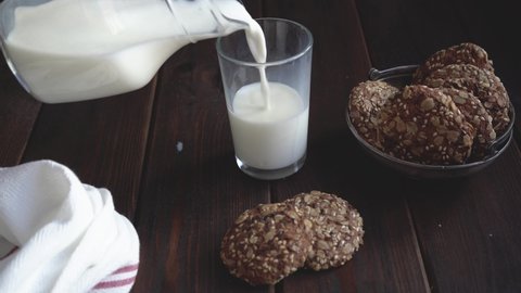 Adding milk into glass. Close up hand holding a milk jug, next to oatmeal cookies.