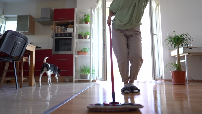 Lovely housewife mops the floor and enjoys music with wireless headphones. Young woman doing house cleaning while dancing