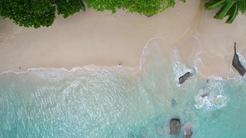 Seychelles, Mahe Island, aerial view from the beach to the ocean, video from a drone, a guy is standing on the beach and the drone is filming him from above	