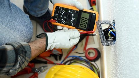 View from above. Electrician worker at work with the tester measures the voltage in an electrical system. Working safely with protective gloves. Construction industry. Footage.