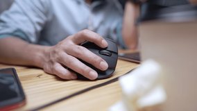 Close up of hand holding black computer mouse on a wooden desk, working equipment with a PC, office working tools, background of people working in modern home office, gamer playing in the video game