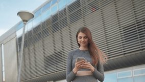 POV of the charming and happy girl. Close-up Of A Beautiful Sports Girl Holding A Smartphone. Close up of the young caucasian woman having a video chat on the modern building background. Outdoors. one