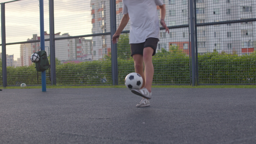 Young caucasian amateur man practicing soccer skills and tricks with the football ball at sunset in an playground. Urban city lifestyle outdoors concept. 4K UHD slow motion RAW graded footage