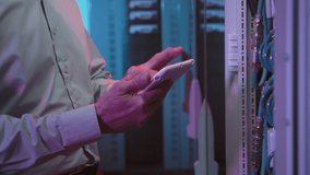 Tilt up close up of middle-aged male data center worker typing on tablet and looking at computing equipment in server room - Powered by Shutterstock - Get 15% off with code: PIKWIZARD15