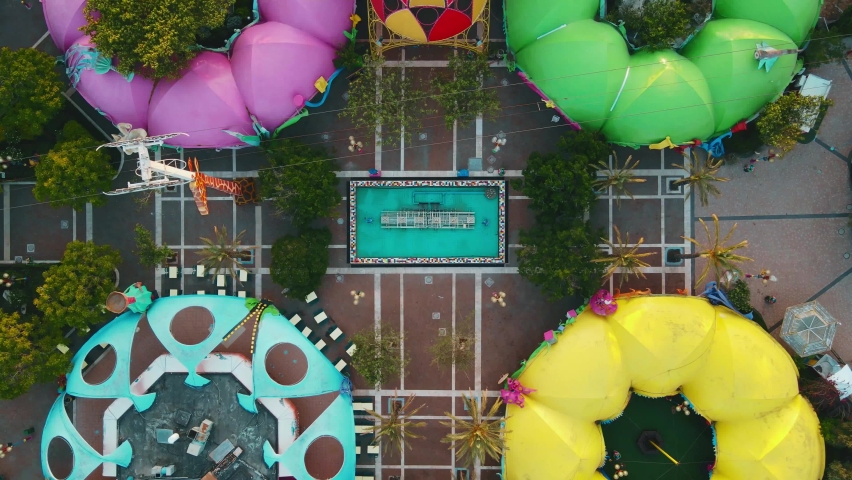 Aerial overhead shot of mushroom shaped buildings in the center of a amusement park with upwards camera motion