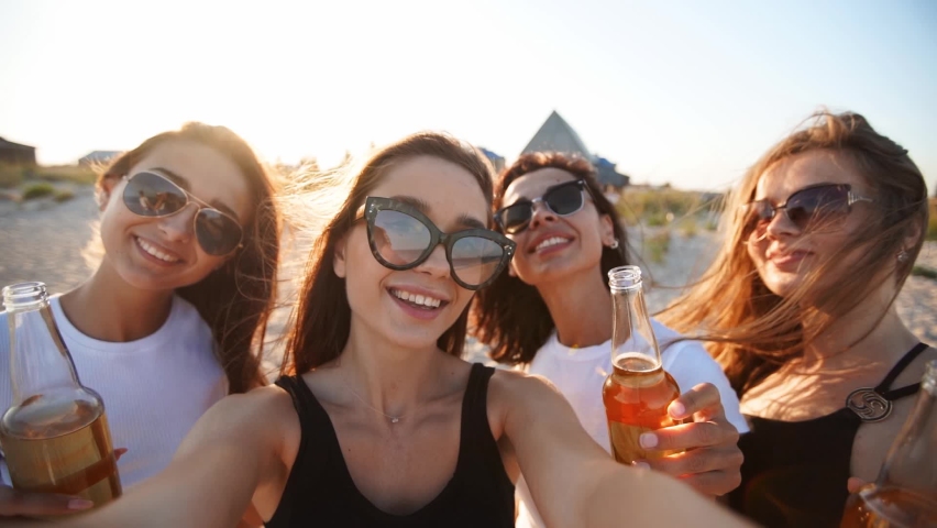 Pov view of pretty women take selfie having fun with drinks on sea beach on sunset. Online video call: girl looking at smartphone camera on tropical island, females toasting bottles, waving hands.