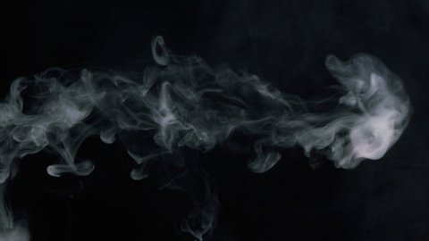 Close-up of smoke rings, smoking hookah or cigarette in dark studio, view side of blowing out puffs of smoke on black background. 