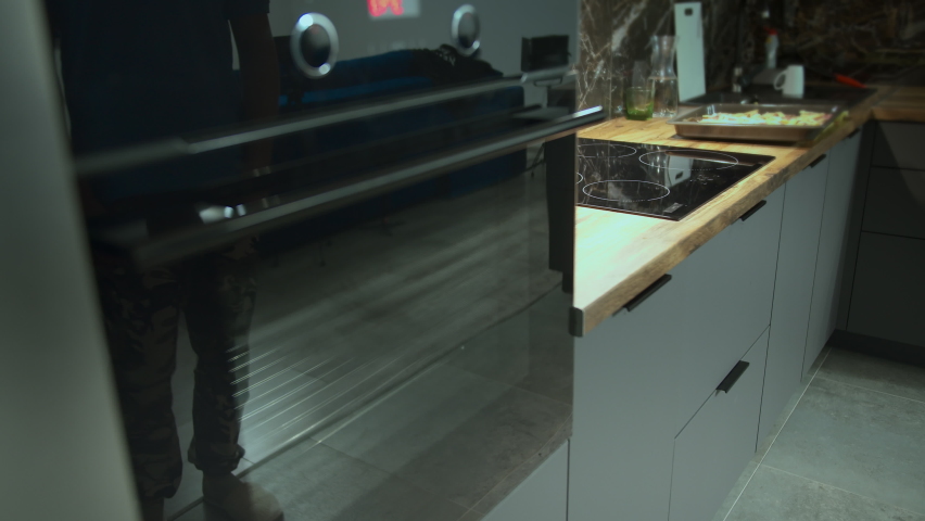 Man opens and puts pizza in the oven to cook, camera tracking