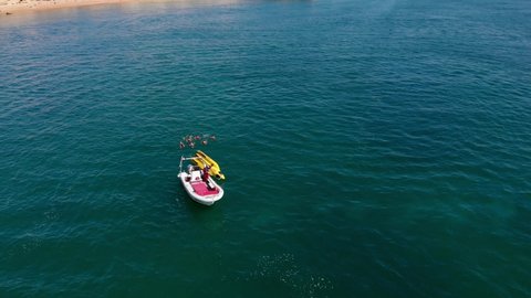 Aerial, static, drone shot, of people swimming towards a inflatable toy, a boat waiting close by, on the coast of Algarve, on a sunny day, in Carvoeiro, Portugal