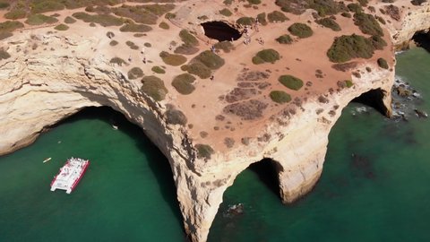 Aerial, reverse, drone shot, overlooking a ferry, a boat and kayaks, at the Benagil cave, on the coast of Algarve, on a sunny, day, in Carvoeiro, Portugal