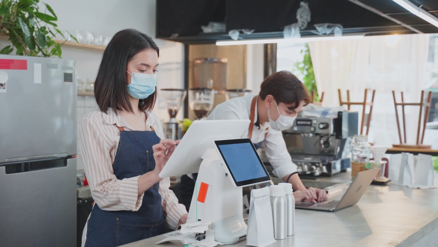 Asian cafe owner couple wear face mask due to Covid19 pandemic, check in sale order from laptop computer on counter bar in restaurant feel happy for income. Entrepreneur and Economic of small business Royalty-Free Stock Footage #1073741306
