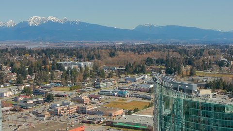 A Snow-Capped Mountain is Juxtaposed with a Modern Glass Condo Tower in Surrey, British Columbia Canada. A Cinematic Drone Orbit on a Sunny Day