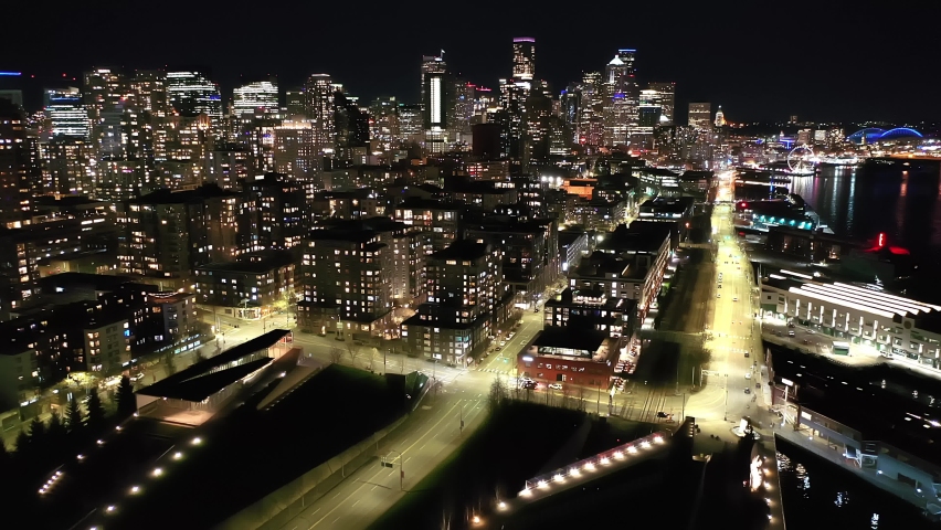 Cinematic 4K drone, after sunset, night footage of downtown Seattle, Washington, Alaskan way waterfront with illuminated streets and offices looking from Elliott Bay Seattle Harbor during blue hour
